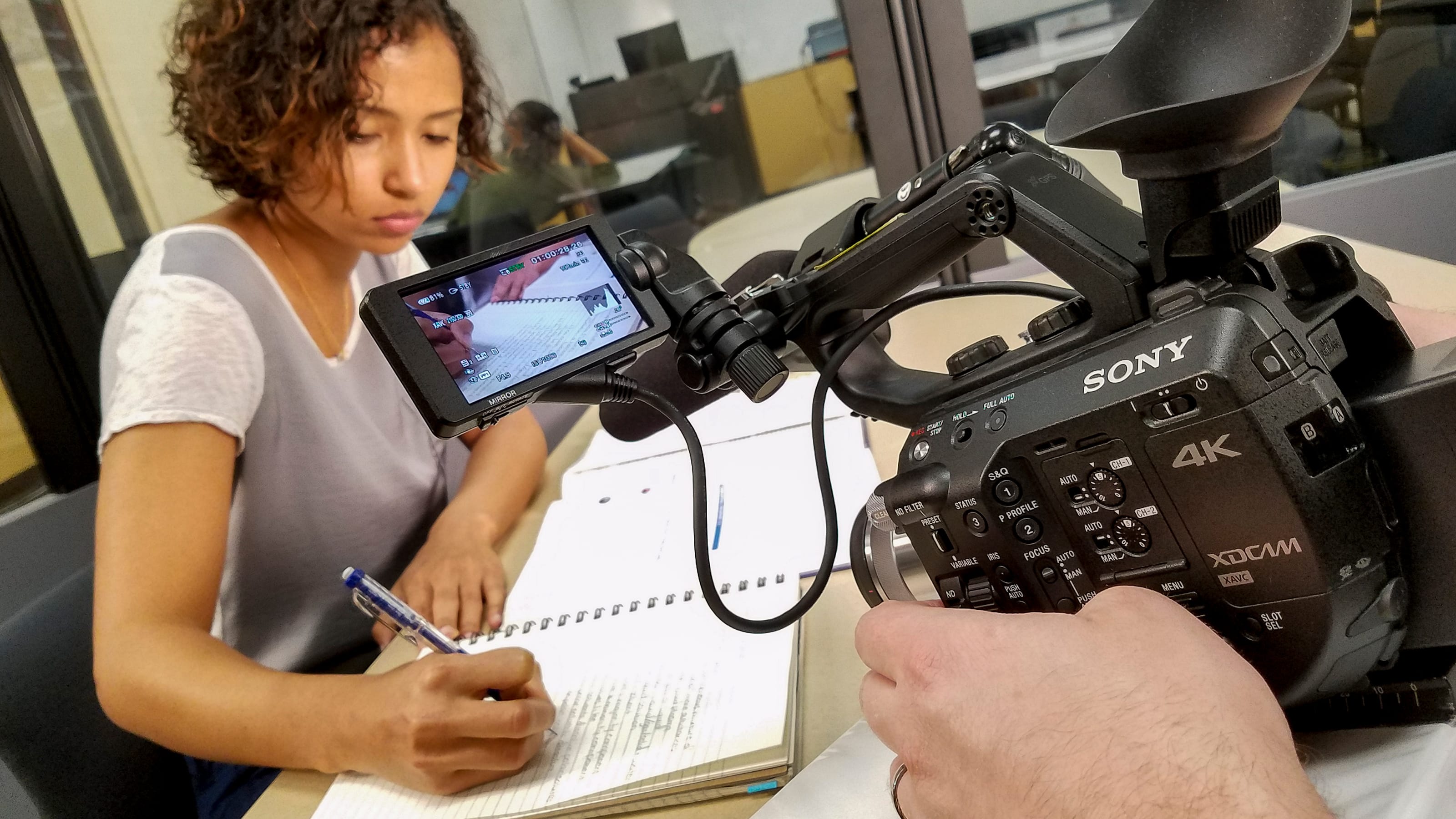 Student writing in a notebook being filmed by camera.