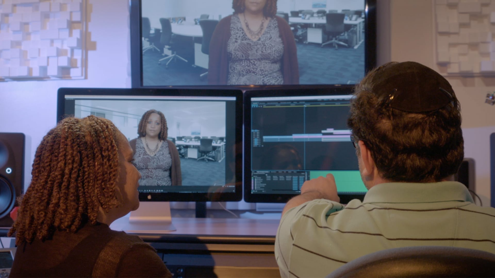 Man and woman editing a video with three computer monitors.